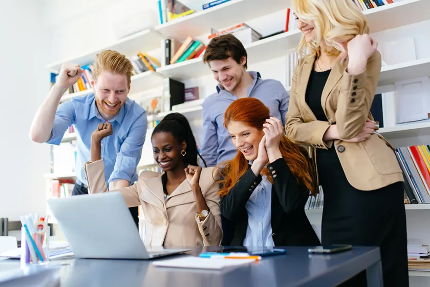 group of people celebrating around laptop in office